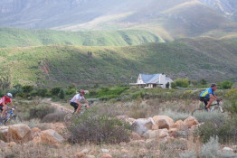 Three participants in the annual Breede River Mountain Bike Race are in the foreground; the Kingsbury Cottage is at the rear.